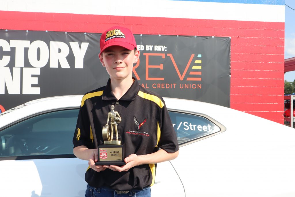 A person holding a trophy in front of a car.