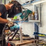 A man welding in an industrial setting with many tools.