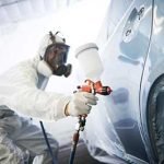 A person in white suit painting a car.