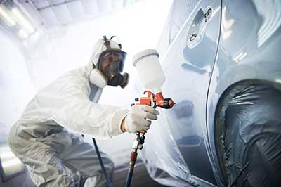 A person in white suit painting a car.