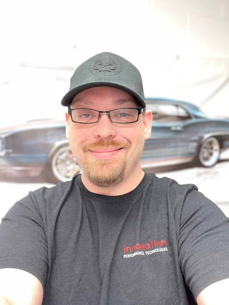 A man wearing glasses and a hat in front of a car.